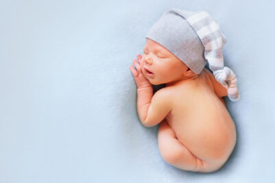 Newborn baby boy in the bonnet sleeping on the light blue background